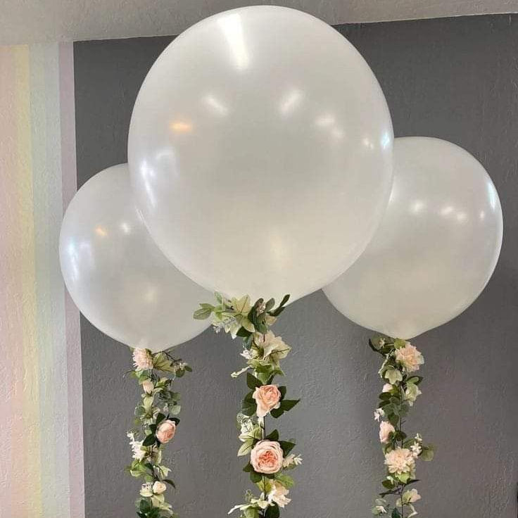 Decorative setup with large white balloons and floral garlands on a plain background