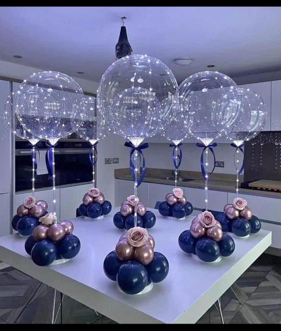 Decorative setup with clear balloons, blue and pink balloons, and flowers on a kitchen counter.