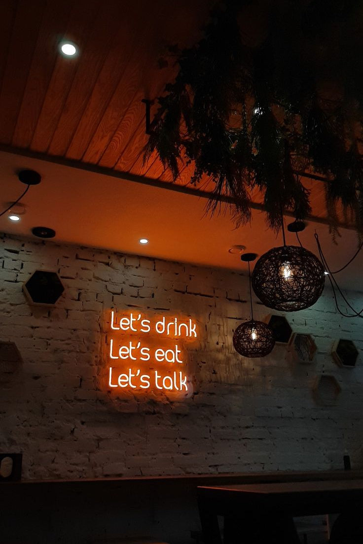 Neon sign with 'Let's drink, Let's eat, Let's talk' text in a dimly lit room.