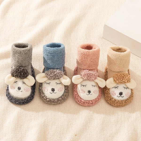 Four pairs of baby booties with sheep face design on a soft fabric background